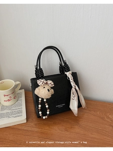 Detail of black pebbled leather handbag featuring floral scarf and cute bear charm