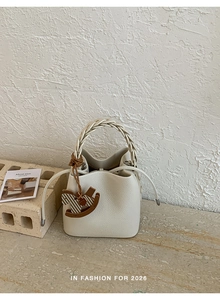 Detail of white lychee leather bucket bag with braided handle and wooden rocking horse charm
