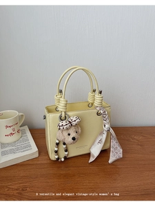 Detailed close-up of cream yellow handbag with bear charm and silk scarf on wooden table