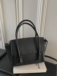 Minimalist black leather trapezoid handbag with thin straps on a premium display base