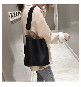 Détail d'un sac seau en cuir noir avec large bandoulière porté par un mannequin en vue