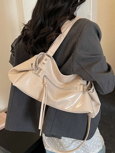 Chic beige glossy shoulder bag with pleated design and fringe tassels on grey blazer