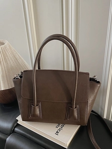Minimalist dark brown leather handbag with round handles and detachable strap on a white stand