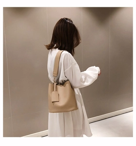 Détail du sac seau beige avec large bandoulière et texture cuir sur une robe blanche