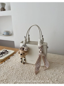 Close-up of cream handbag with braided handle detail, floral scarf and plush bear charm