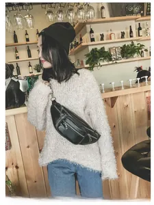 Détail d'un sac banane en cuir noir avec zips argentés porté sur un pull blanc moelleux