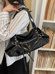 Glossy black underarm bag with silver zipper detail on a minimalist bookshelf background