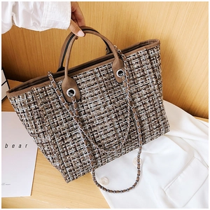 Detail of tweed tote bag with chain strap on wooden surface in warm lifestyle setting