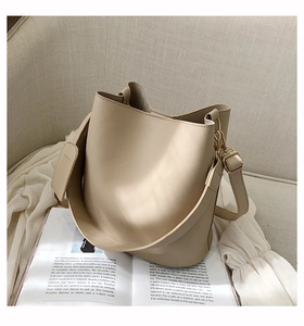 Détail d'un sac seau blanc crème avec large bandoulière et ferrures dorées sur un canapé