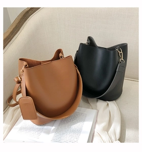 Détail des sacs seau en cuir marron et noir avec larges bandoulières sur un canapé