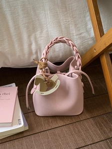 Pink lychee leather bucket bag with woven handle and trojan charm on a wooden background