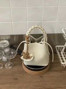 Minimalist beige leather bucket bag with woven handle and rocking horse charm decoration