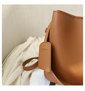 Détail d'un sac seau en cuir marron montrant la texture fine et les boucles dorées