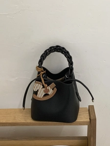 Minimalist black leather bucket bag with woven handle and rocking horse charm on wood shelf