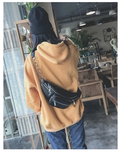 Détail d'un sac banane en cuir noir avec chaîne argentée porté en bandoulière sur le dos