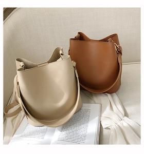Vue de dessus de deux sacs seaux en cuir mat beige et marron sur un canapé en tissu