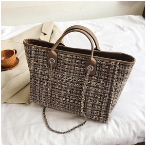 Detail of woven tweed tote bag with brown leather handles and silver chain accents