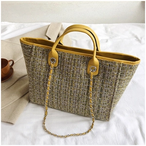 Macro detail of yellow tweed tote bag with metal chain strap and leather handle