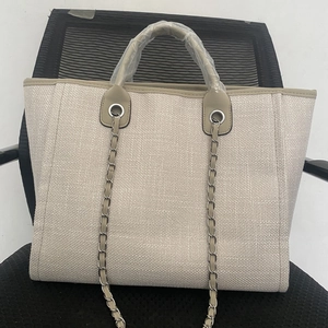 Detail of beige woven tote bag featuring khaki leather trim and metal chain strap