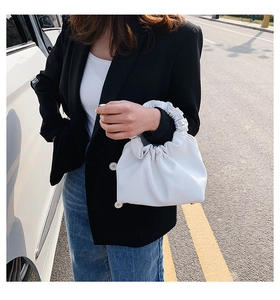 Outdoor shot of white pleated cloud bucket bag featuring unique ruched handle and sleek leather finish