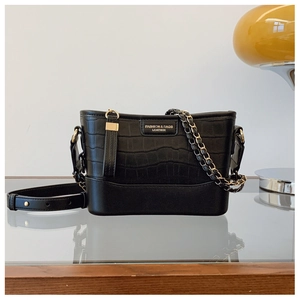 Macro shot of black crocodile pattern bucket bag with gold chain and leather strap