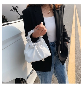 Detail shot of a white ruched cloud bag held by a model in casual outdoor street setting