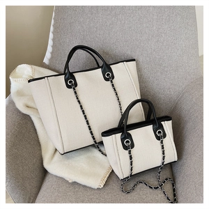Macro shot of two canvas tote bags in different sizes with black leather trim and chain strap