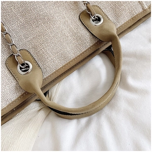 Detail of woven beige tote bag featuring chain link shoulder straps and padded handles