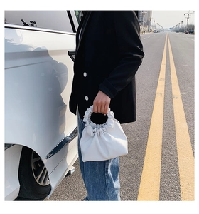 Detail of a white pleated cloud-style bucket bag with integrated circular soft handle