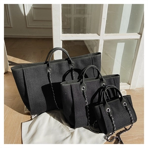 Three-piece black bucket tote bag set with chain straps on a sunlit wooden floor
