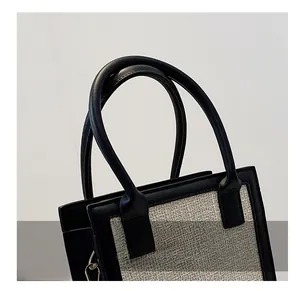 Detailed close-up of woven gray handbag with black leather handles and metal hardware