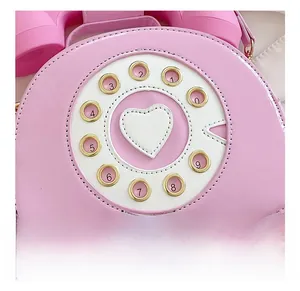 Close-up of pink telephone-shaped bag featuring a white heart and golden dial details