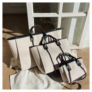 Three sizes of canvas tote bags with black leather trim and chain handles set on wood floors