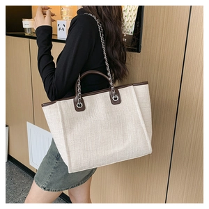 Close-up of cream woven tote bag with dark brown leather trim and silver chain strap
