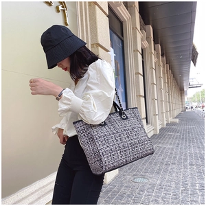 Close-up of black and white tweed tote bag with metal chain strap and leather trim