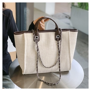 Outdoor close-up of a woven tote bag with brown leather trim and chain strap on a table