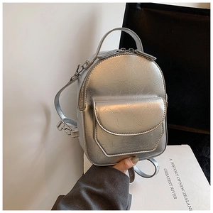 Dettaglio di un mini zaino in pelle metallizzata argento tenuto in mano per le dimensioni