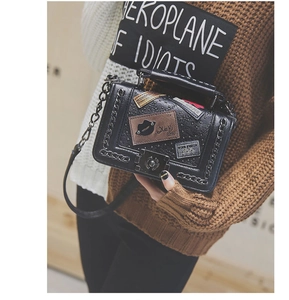 Detail of black glossy leather crossbody bag with chain trim and decorative metal patches