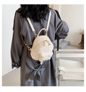 Detail of a beige quilted mini backpack with gold hardware worn on a model's back