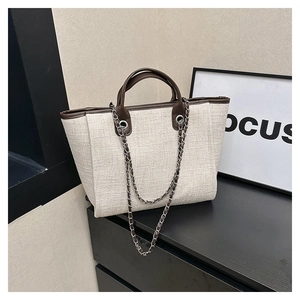 Close-up of cream tweed tote bag with brown leather handles and silver chain detail