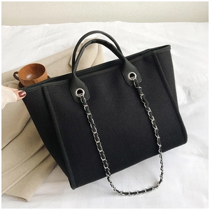 Close-up of large black canvas tote bag with leather handles and silver chain strap