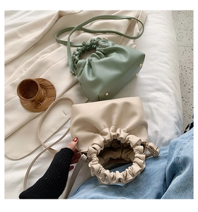 Detail of soft leather bucket bags in sage green and cream with pleated handle on bed