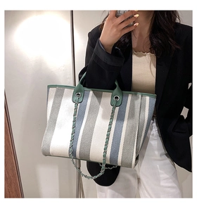 Détail d'un sac cabas en toile rayée avec poignées vertes et bandoulière en chaîne métal