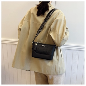 Detail of a black faux crocodile leather crossbody bucket bag with a metal logo plaque