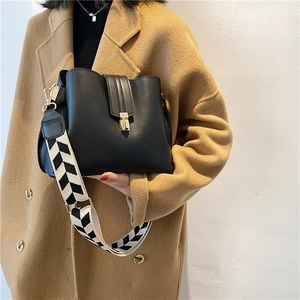 Black leather bucket bag with geometric wide strap shown on a camel wool coat