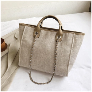 Detail of beige canvas tote bag with khaki leather trim and metal chain strap