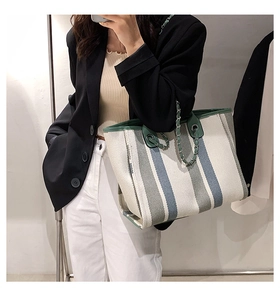 Détail du grand sac cabas en toile rayée avec bandoulière chaîne porté par un mannequin