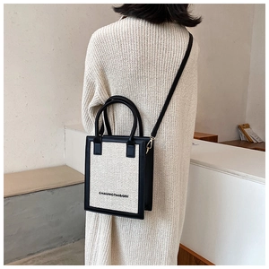 Detailed view of cream canvas crossbody bag with black leather trim worn by a model