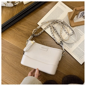 Detail of white crocodile pattern hobo bag with gold chain strap on a wooden table