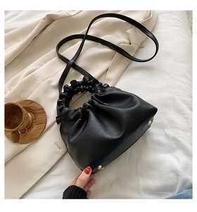 Detail view of black pleated bucket bag with matte texture and golden bottom studs